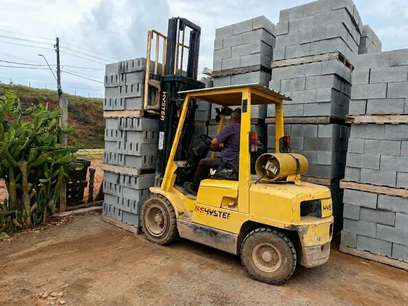 Empilhadeira amarela junto a pilhas de blocos de concreto em paletes.