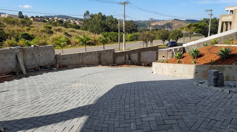 Piso intertravado cinza em área externa cercada por muretas, com terreno e rua ao fundo.