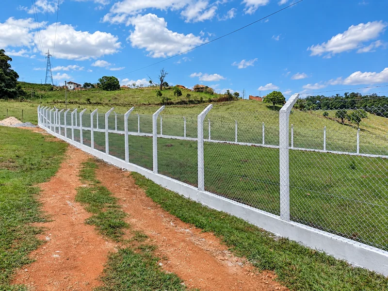 Sequência de mourões de concreto e tela de alambrado acompanhando um caminho de terra