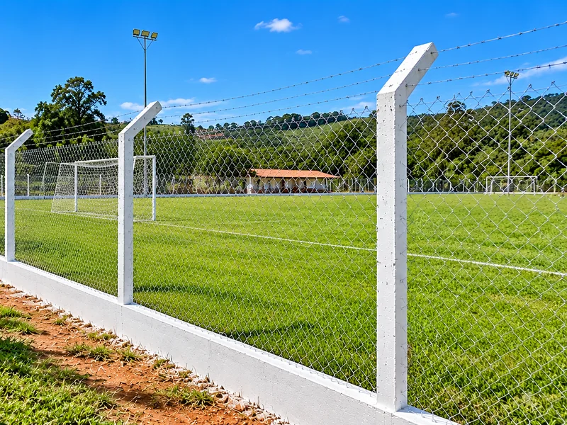 Alambrado com mourões de concreto ao redor de um campo gramado com traves